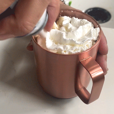 Whipped cream, chocolate shavings, and a red raspberry are added to the Raspberry Mocha Latte inside an Ember Mug 14 oz in Rose Gold.