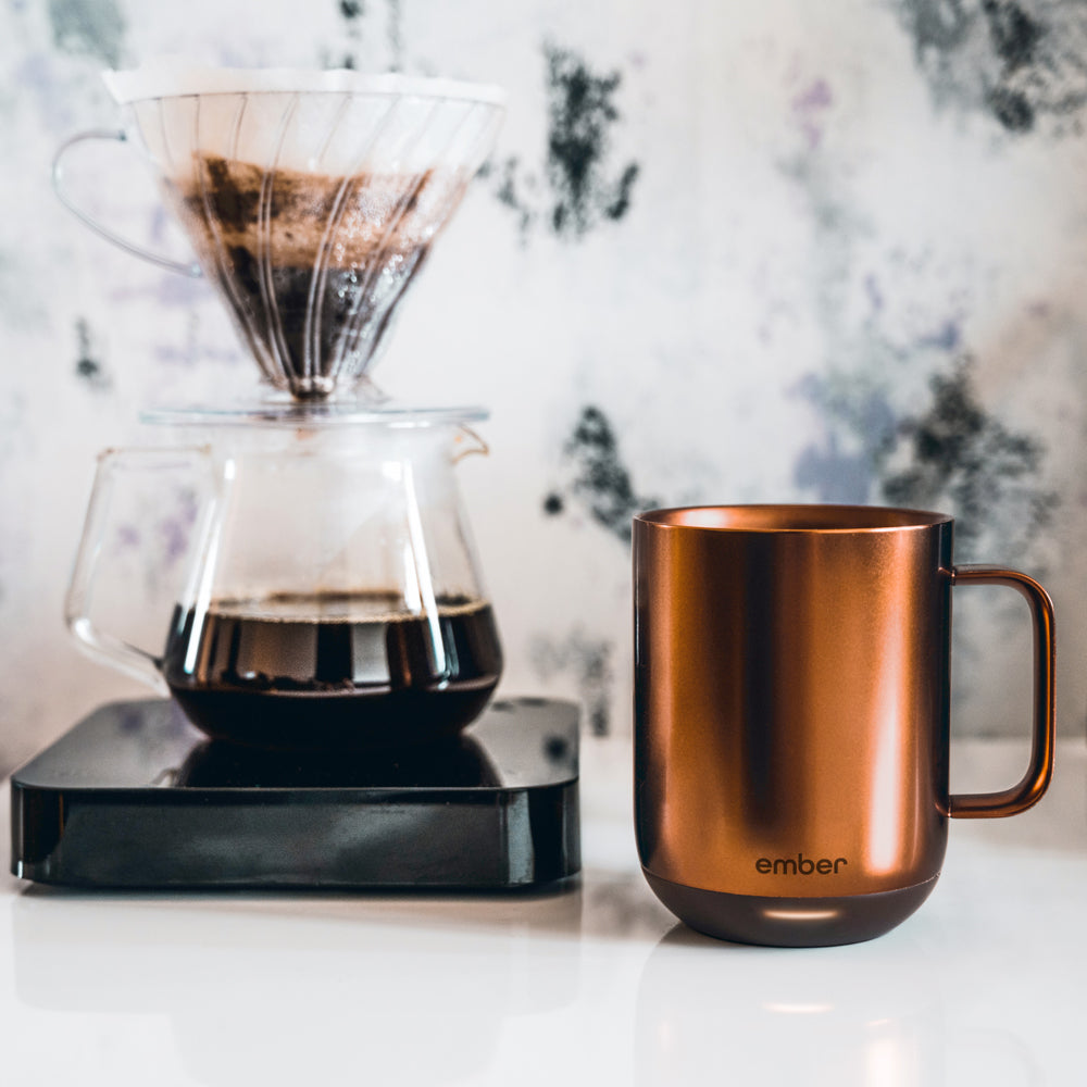 Ember Mug²: Copper Edition sits next to a Hario V60 is a pour over coffee brewer filled with coffee.