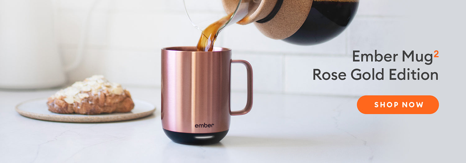 Coffee being poured into an Ember Mug² in Rose gold with a baked good in the background.