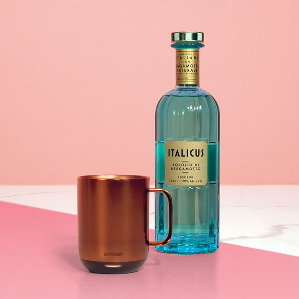 Ember Mug²: Copper Edition next to a blue bottle of Italicus Bergamot Liquor on a pink background.