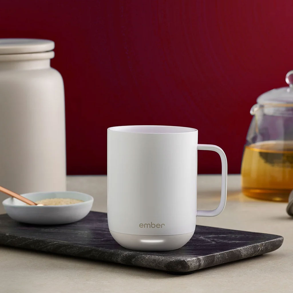 A white Ember Mug² sits next to a glass teapot filled with warm black tea.
