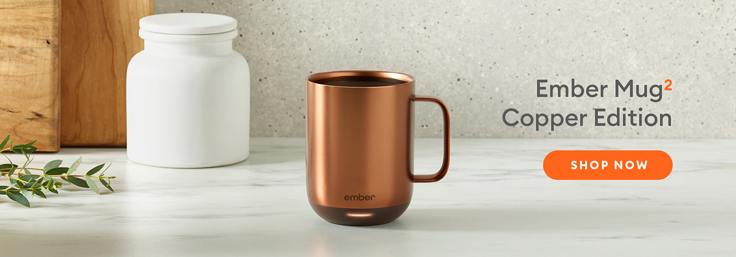 Ember Mug²: Copper Edition resting on marble countertop with wooden cutting boards and a eucalyptus branch in the background.